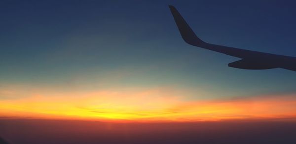 Silhouette airplane flying against sky during sunset