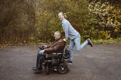 Cheerful young man riding on motorized wheelchair of retired senior father with disability