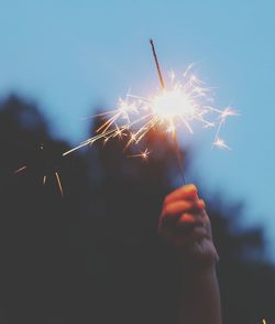 Cropped hand holding lit sparkler at night