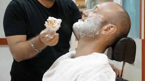 Barber applying shaving cream on mature man in salon