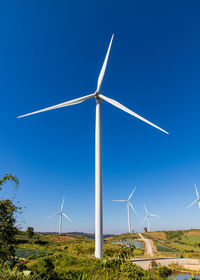 Low angle view of wind turbines on field against clear blue sky