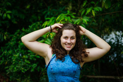 Portrait of smiling young woman with hand in hair against tree