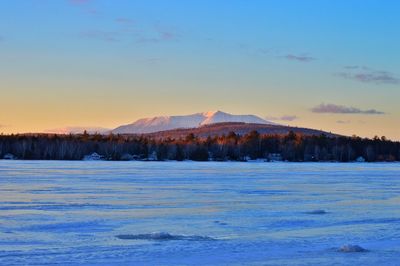 Distant view of mt katahdin by frozen lake against sky during sunset