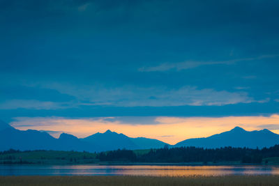 Scenic view of lake against cloudy sky during sunset