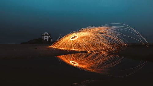 Illuminated spiral sparks by beach against sky at night