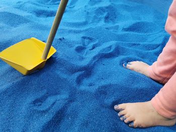 Small child feet playing with shovel in blue sand.