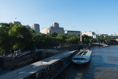 Bridge over river by buildings against clear blue sky