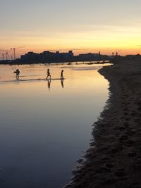 Silhouette people on beach against sky during sunset