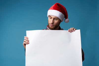 Young man wearing santa hat holding placard against blue background