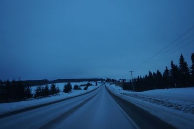 Road amidst trees against clear blue sky during winter