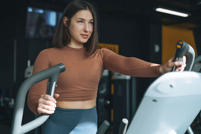 Young smiling brunette woman training for cardio equipment at fitness gym