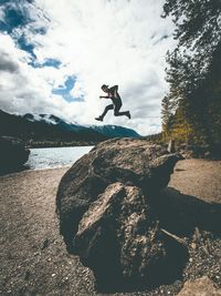 Scenic view of a man jumping over a stone