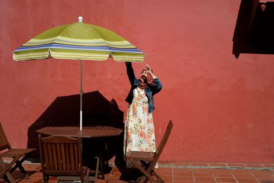 Woman adjusting umbrella while standing against wall