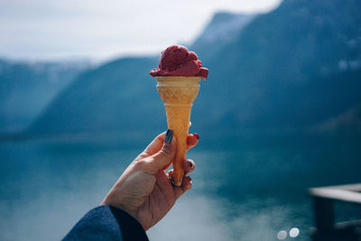Cropped hand of woman holding ice cream cone against lake