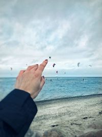 Optical illusion of cropped image of woman touching kite flying over sea against cloudy sky