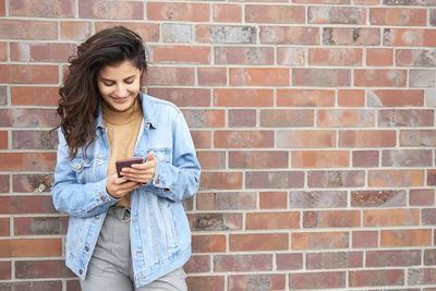 Teenage girl looking away while standing against brick wall
