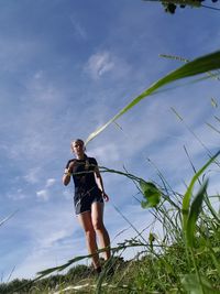 Low angle view of woman running on grassy field against blue sky