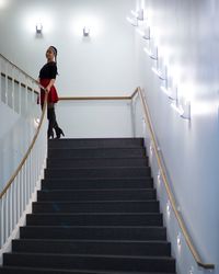 Young woman standing on staircase against white wall