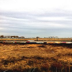 Railroad tracks on field against cloudy sky