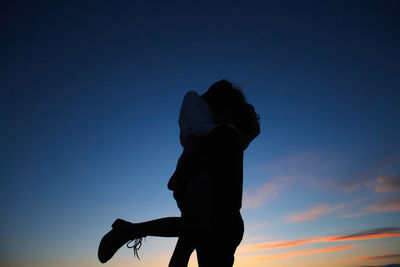Young lovely couple hugging each other and kissing at orange sunset. silhouette at sunset background