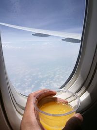 Cropped hand of person holding juice by airplane window