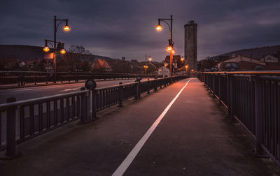 Illuminated street lights on bridge in city at dusk