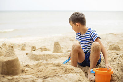 Side view of boy playing with sand at beach