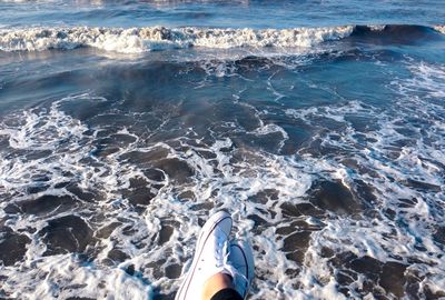 Low section of woman wearing shoes against sea