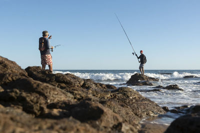 Men fishing on rock by sea against sky