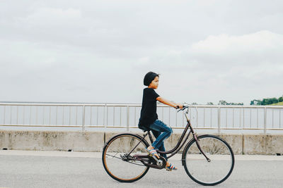 Man riding bicycle on railing against sky