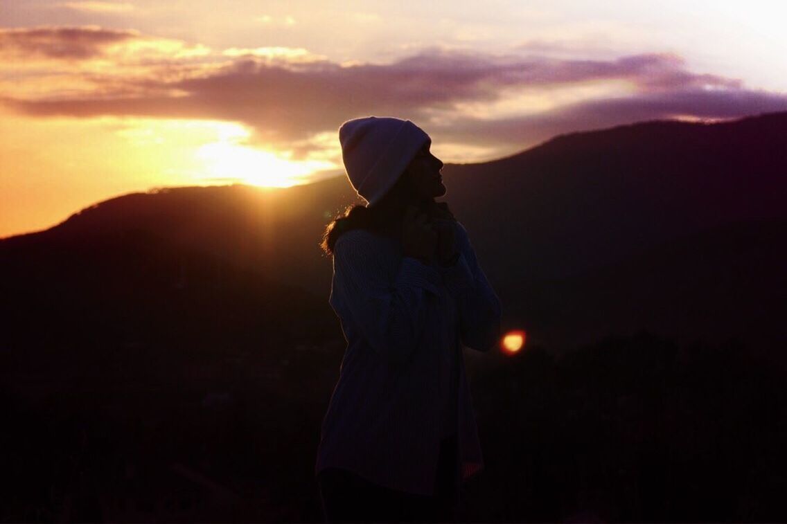 MAN STANDING ON SHORE AGAINST SKY DURING SUNSET