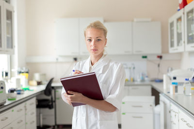 Portrait of woman holding book standing at laboratory