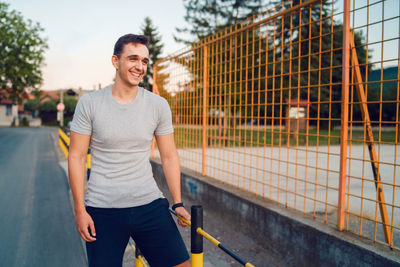 Smiling young man standing by railing on road