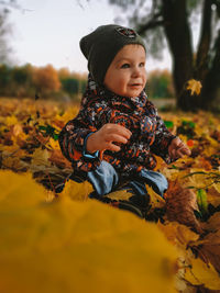 Cute boy sitting on leaves during autumn