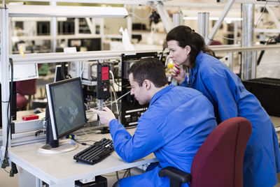 Male electrician pointing at computer monitor while discussing with colleague in industry