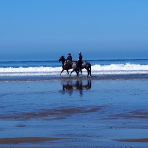 Man and woman riding horses on beach at newgale