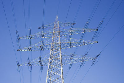 Low angle view of electricity pylon against clear blue sky