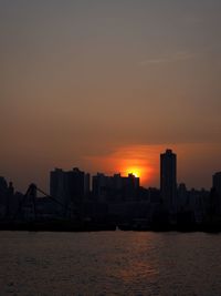 Sea by cityscape against sky during sunset