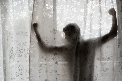 Man with arms outstretched standing in balcony seen through curtain