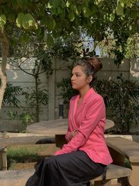 Young woman looking away while sitting on tree