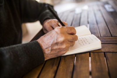 Elderly man writing in his notebook on the porch of his house