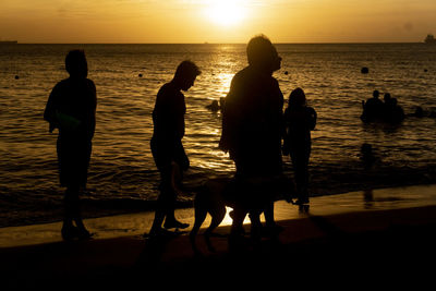 Silhouette people on beach against sky during sunset