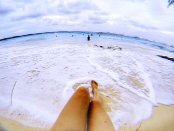 Low section of person on beach against sky