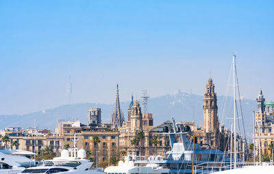 Sailboats in harbor by buildings against sky in city