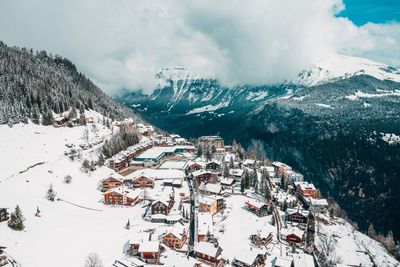 High angle view of buildings on snow covered mountain against cloudy sky during winter