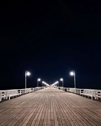 Empty footpath along illuminated street lights at night with stars