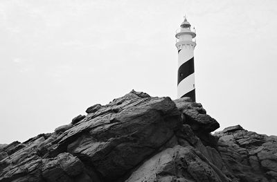 Low angle view of lighthouse on rock by building against sky