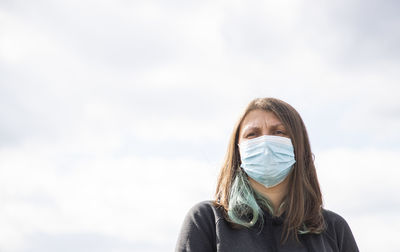 Low angle view of woman wearing mask standing against fence