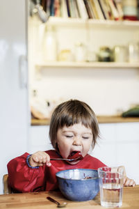 Little girl eating fruit salad at table in house