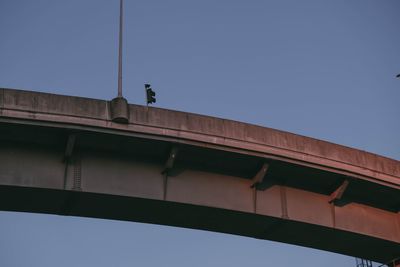 Low angle view of bridge against building against clear blue sky